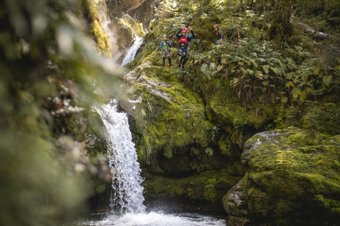 Man jumping off a waterfall surrounded by lush greenery