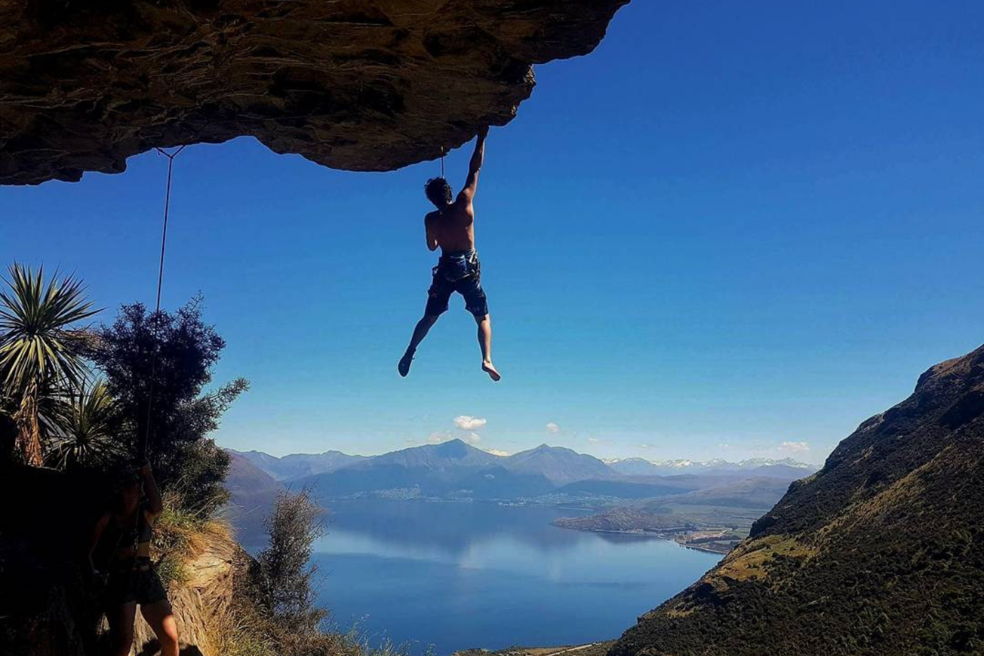 Rockclimber hanging off rock above lake and mountains