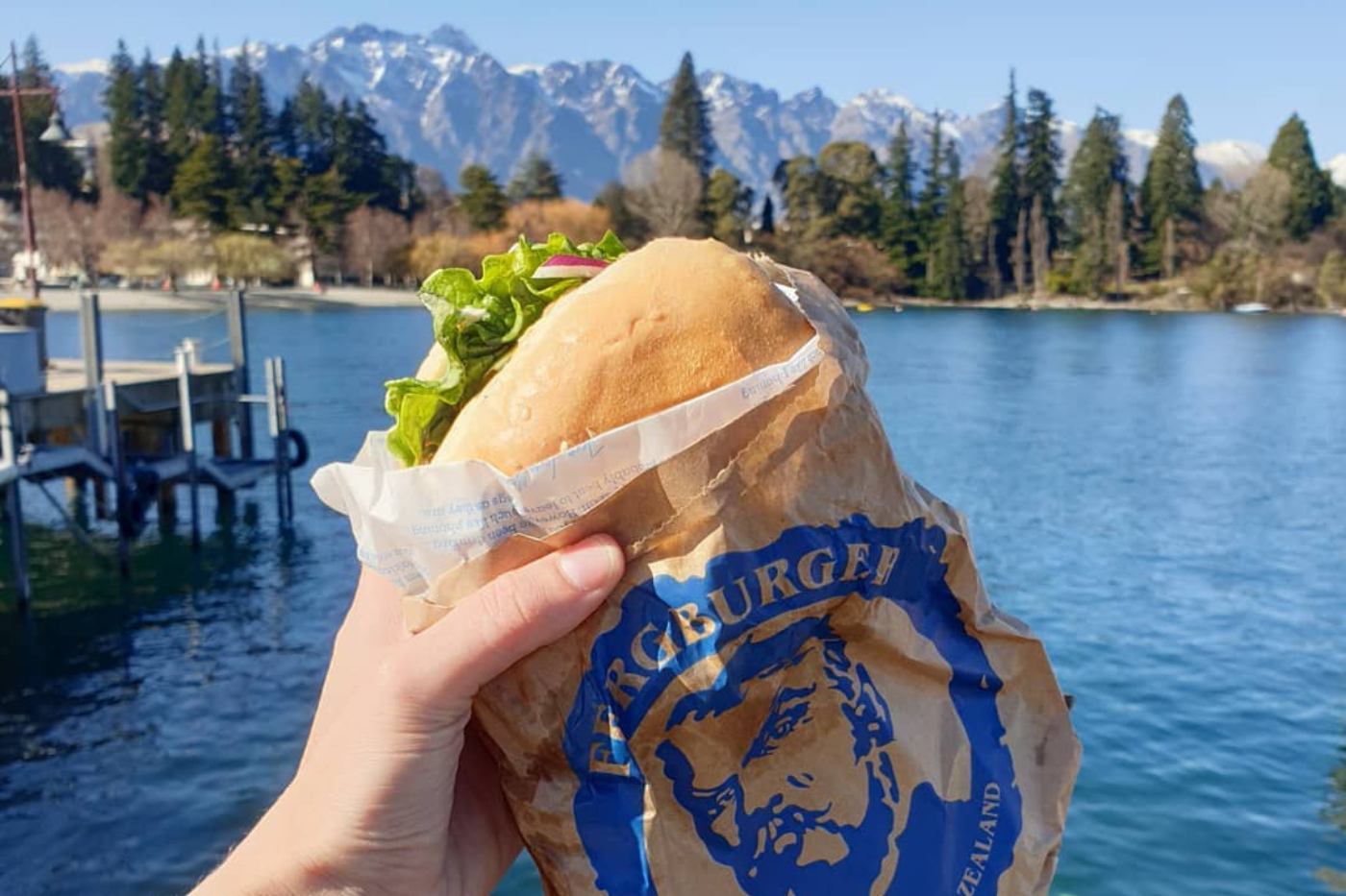holding burger in front of lake and mountains