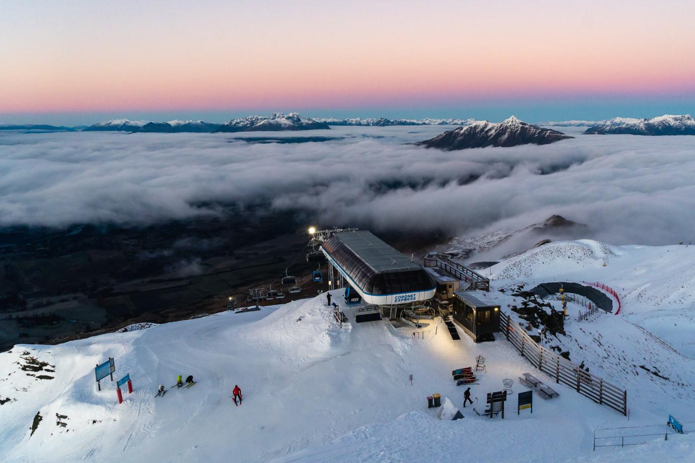 Soft warm hues of the sunrise at Coronet Peak with mountain poking out above clouds