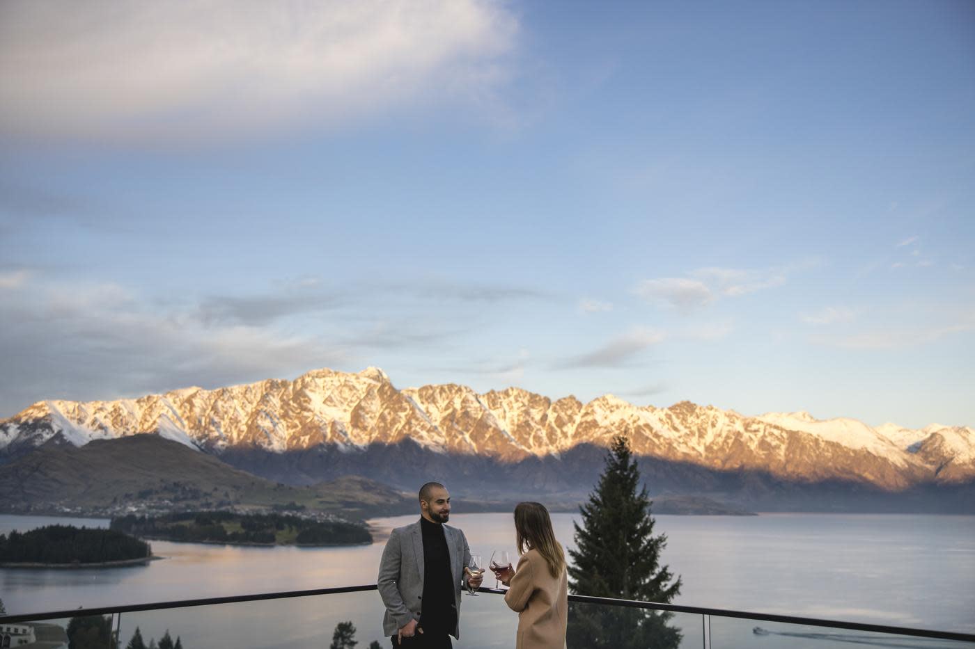 People enoying a wine on the balcony of Nest Kitchen and Bar overlooking the snow-covered Remarkables mountain range