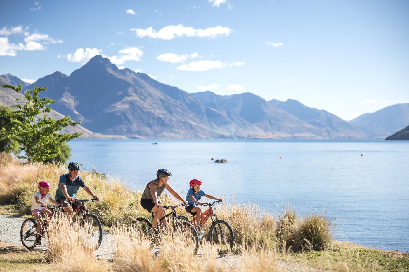 A Family biking around the Queenstown Gardens, with Lake Whakatipu and Cecil Peak in the background