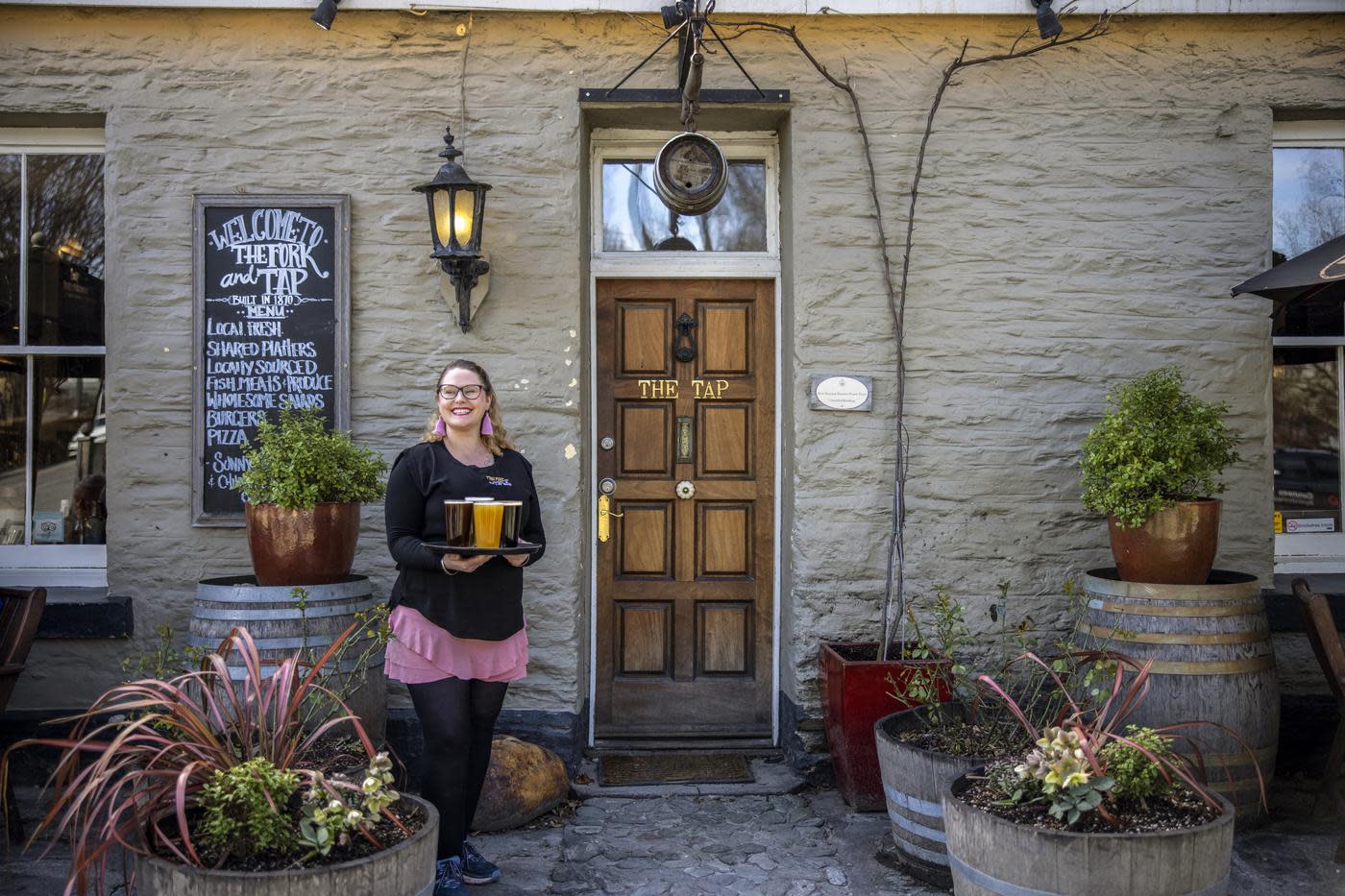 Person with tray of beer standing in front of the Fork and Tap pub Arrowtown