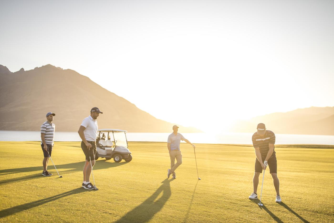 four men playing golf at Jacks Point golf course at sunset with lake and mountains in the background