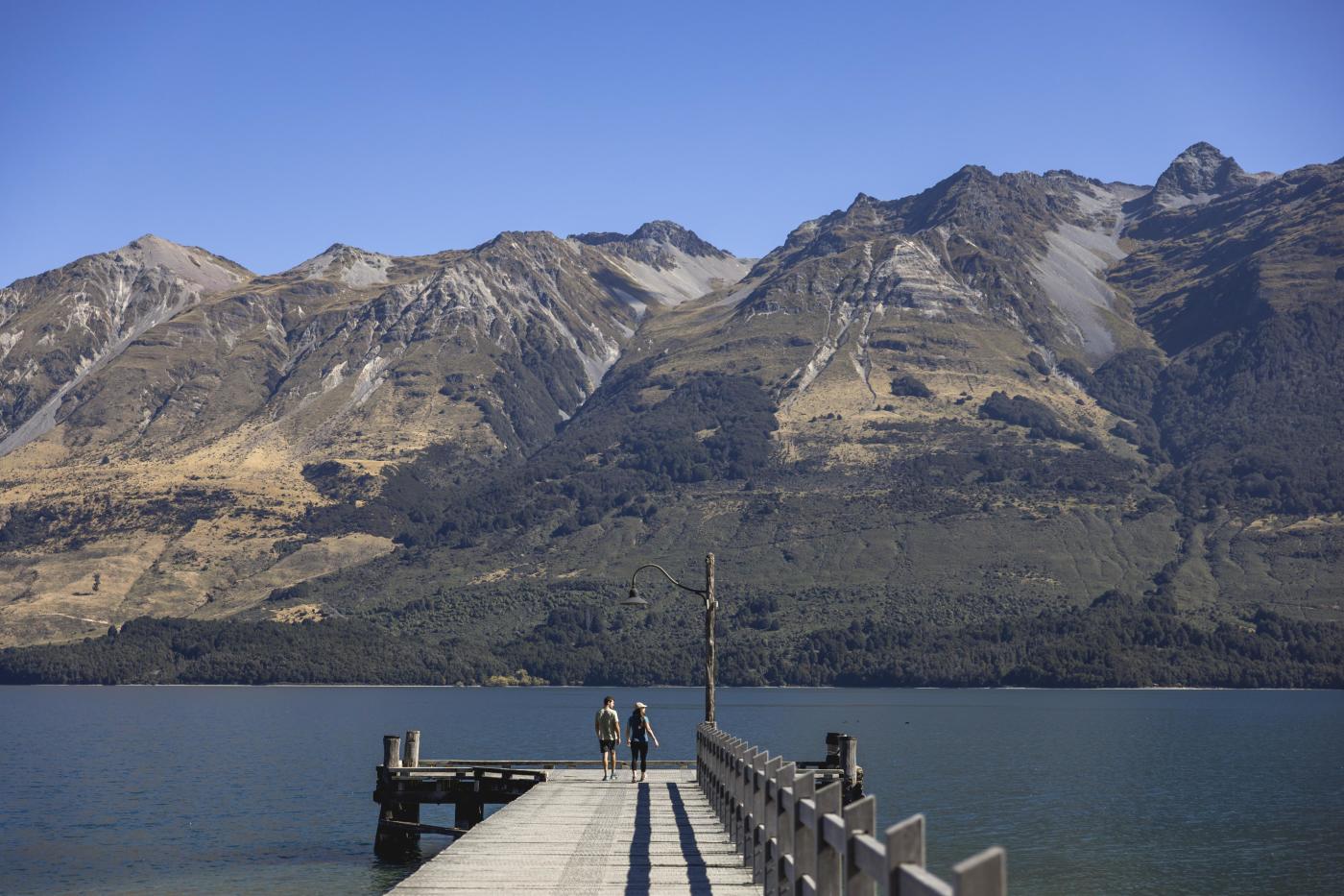 Two people standing on Glenorchy Wharf with mountains in the background