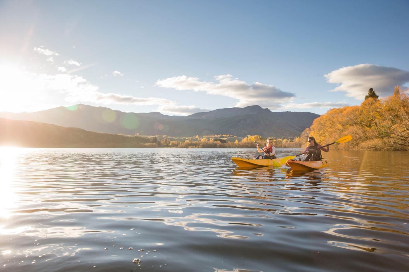 Two frineds kayaking on a lake with yellow autumn trees in the background