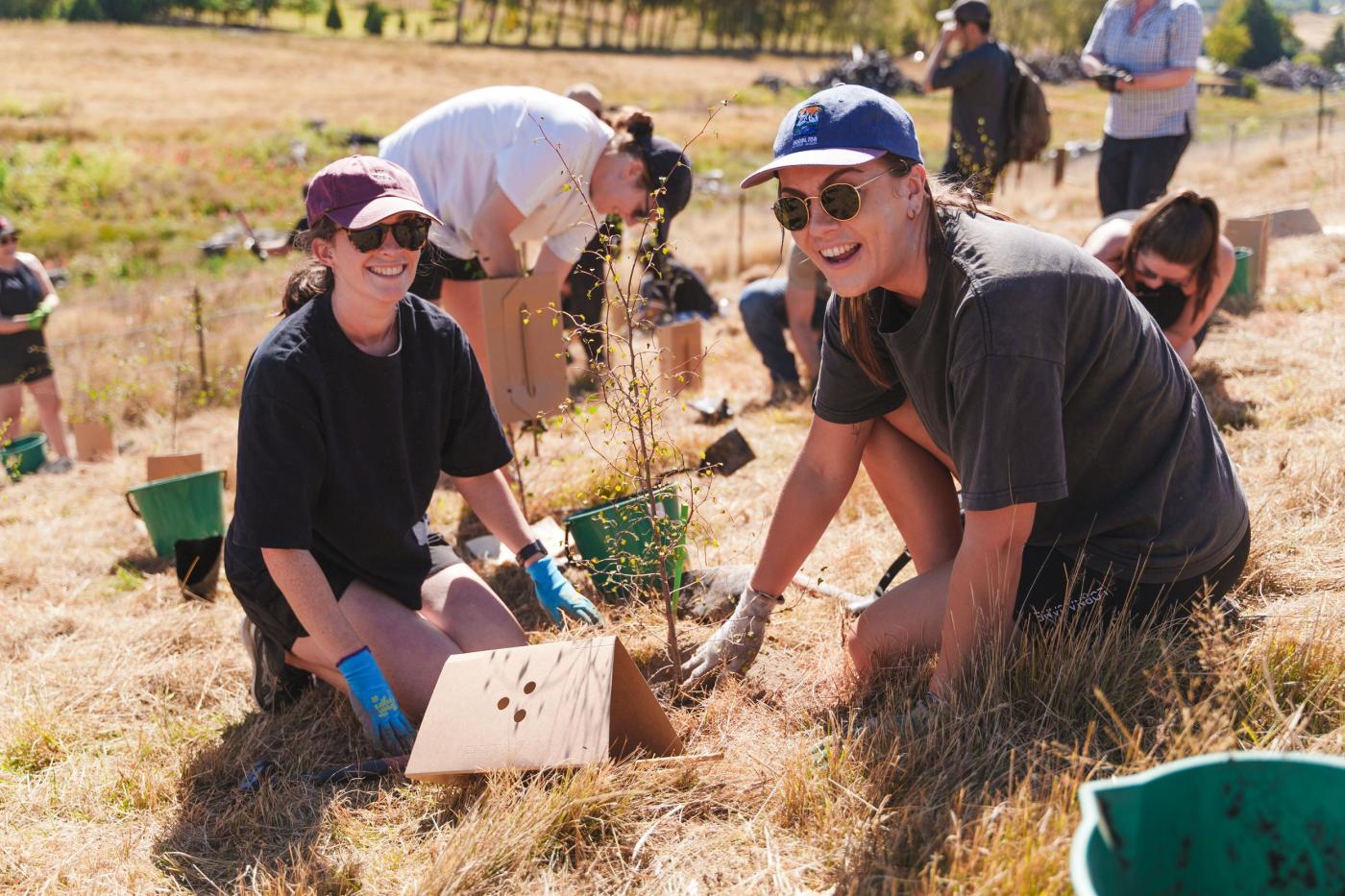 Two women smiling as they plant trees at a Love Queenstown Industry Planting Day