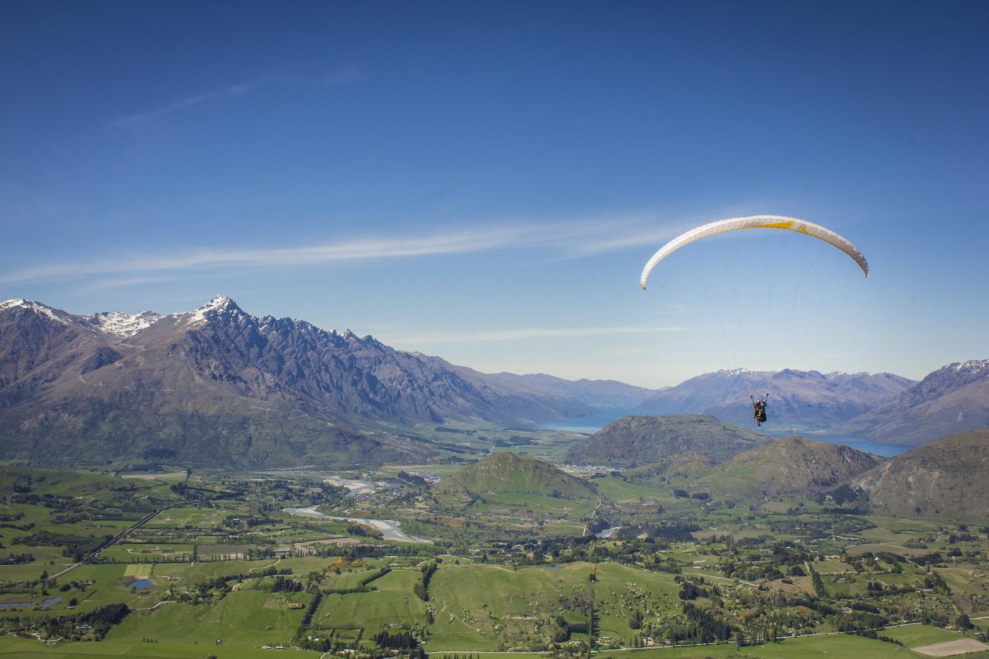 Hang Gliding at Coronet Peak in spring over green valley with the Remarkables in the background