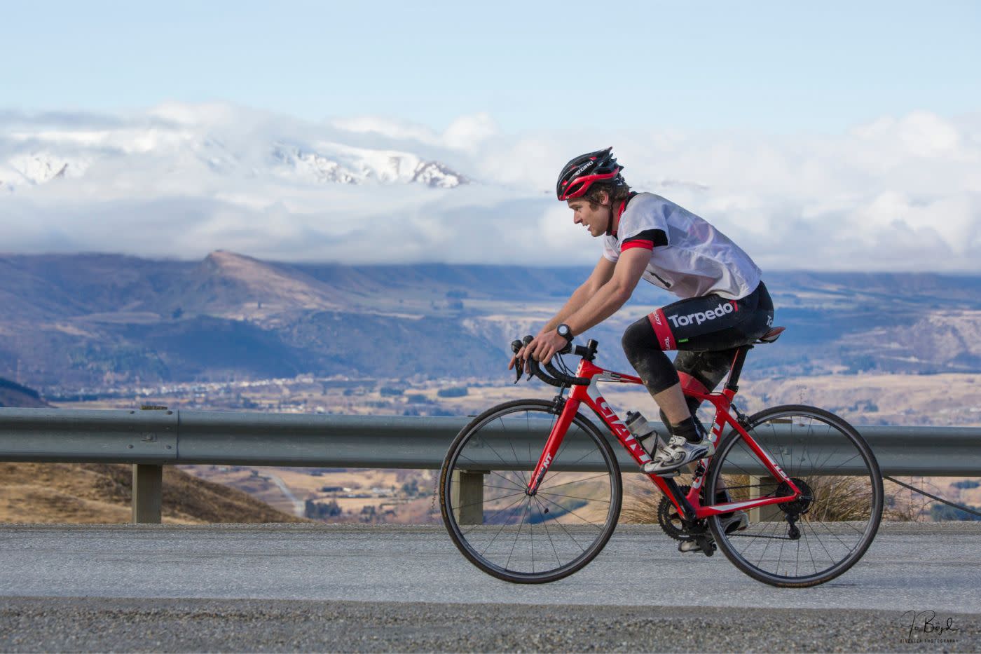 Athlete Hamish Fleming biking on road with snowy mountain backdrop during Peak to Peak adventure race