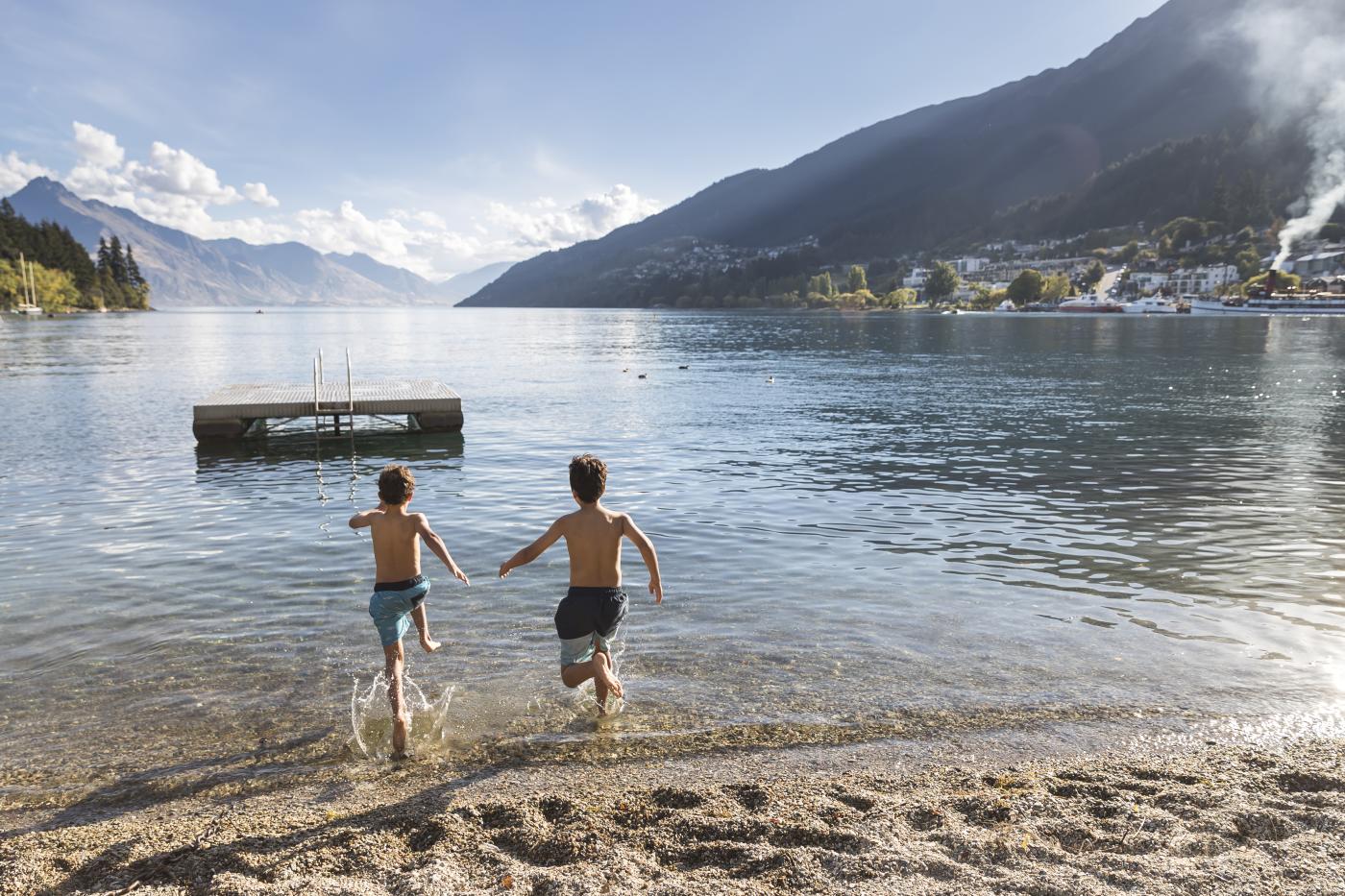 Young boys running into the water at Queenstown Bay in summer