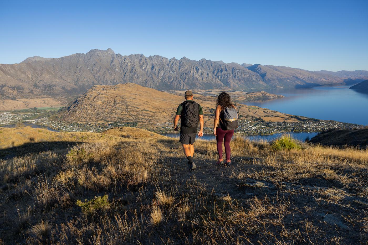 Two people walking with the Remarkables mountain range in the background
