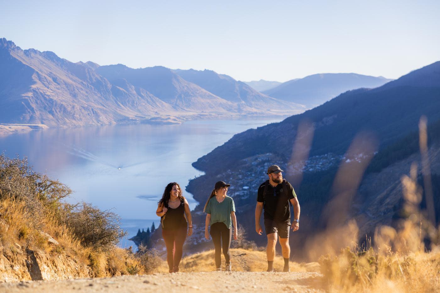 Three people walking on a steep track with mountains and lake views in the background