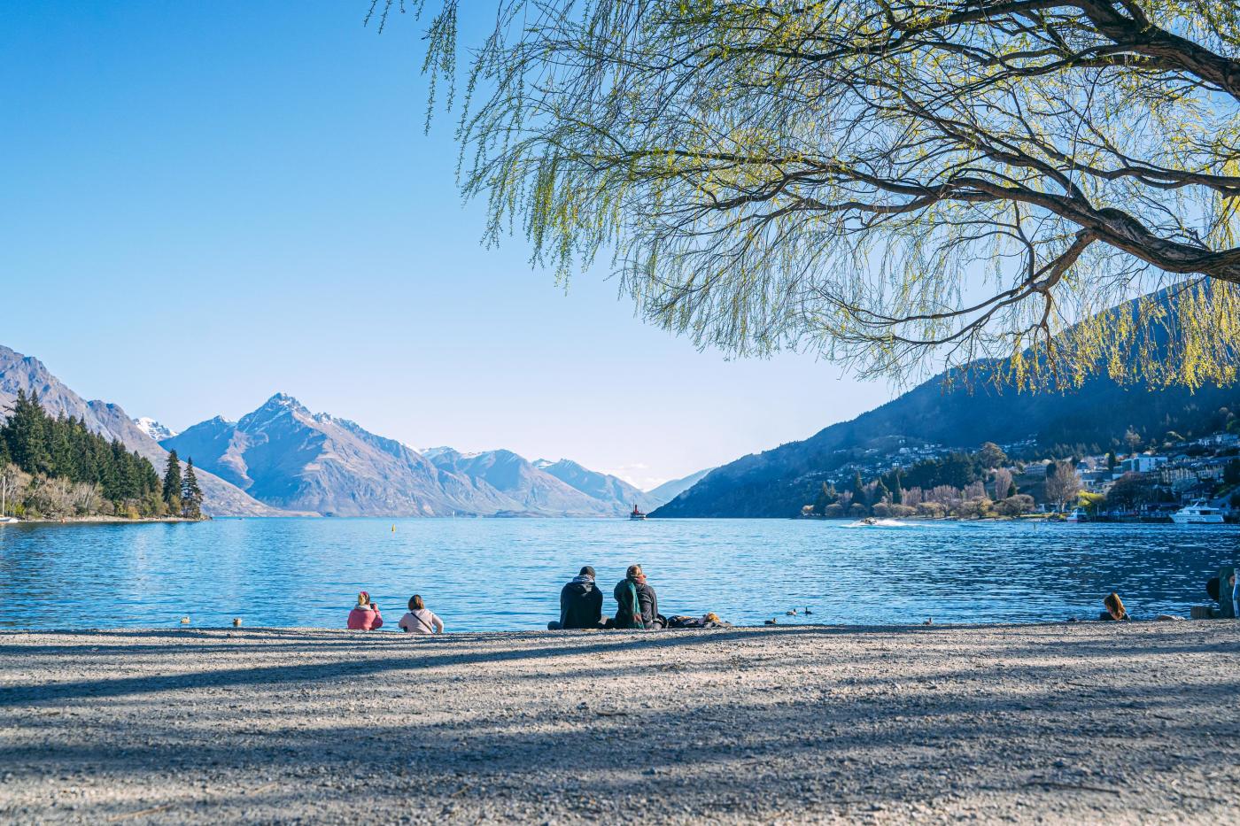 People sitting on Queenstown beach in spring with lake views and mountains in the background