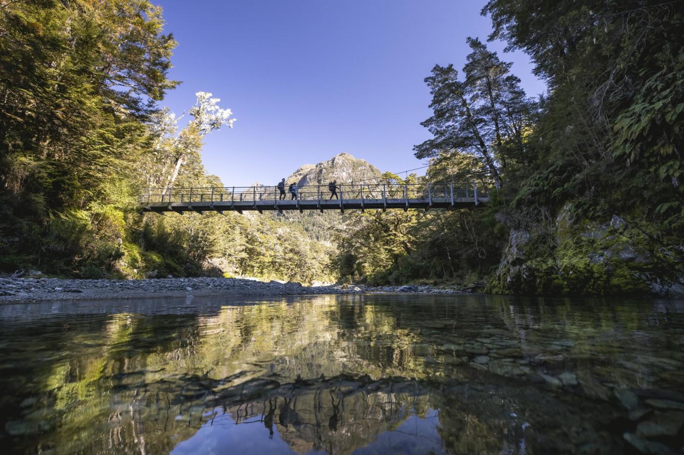 Ground of friends crossing a swing bridge on the Routeburn Track with a mountain in the background