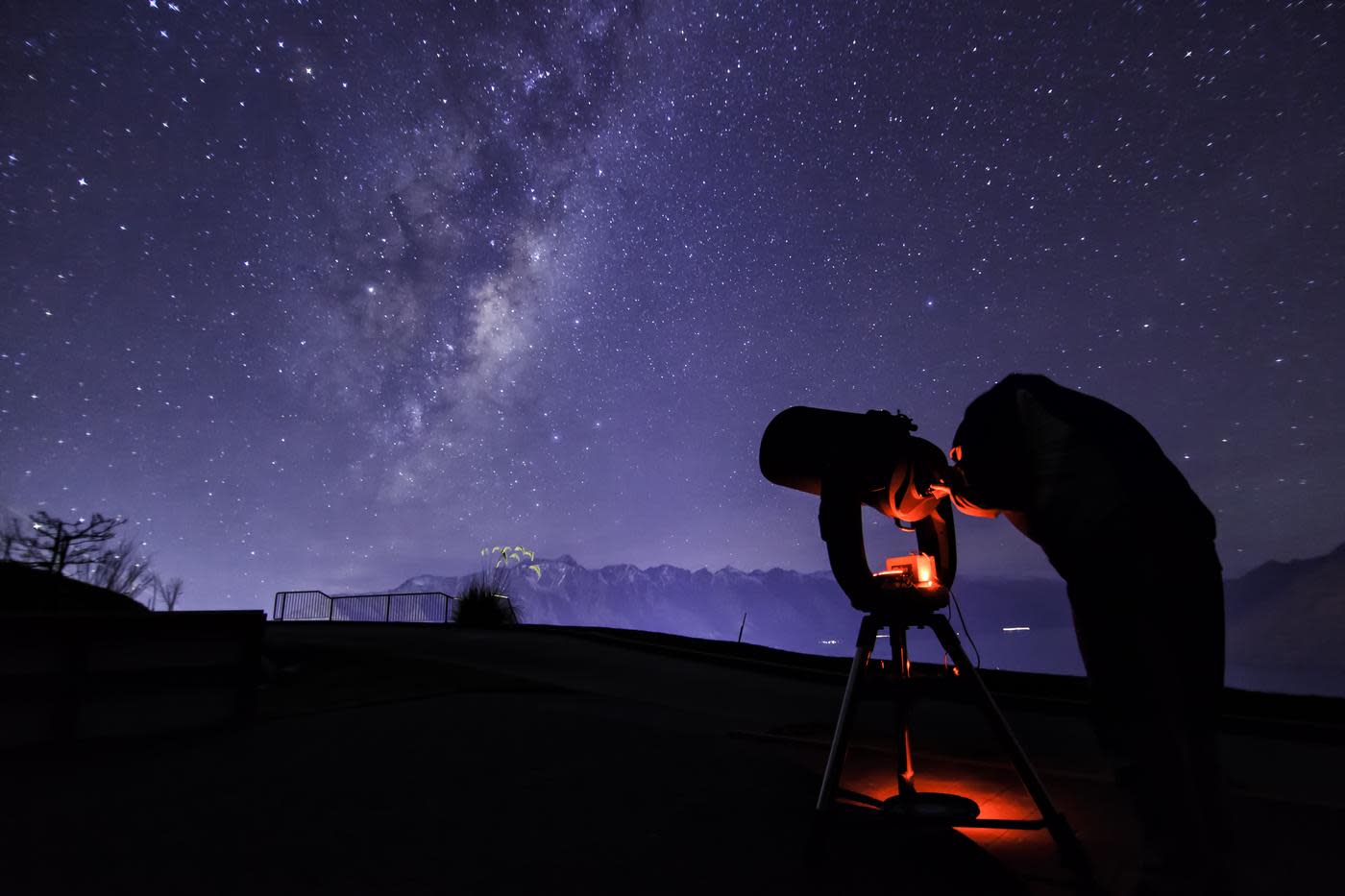 Person with telescope stargazing underneath the milky way near The Remarkables mountain range