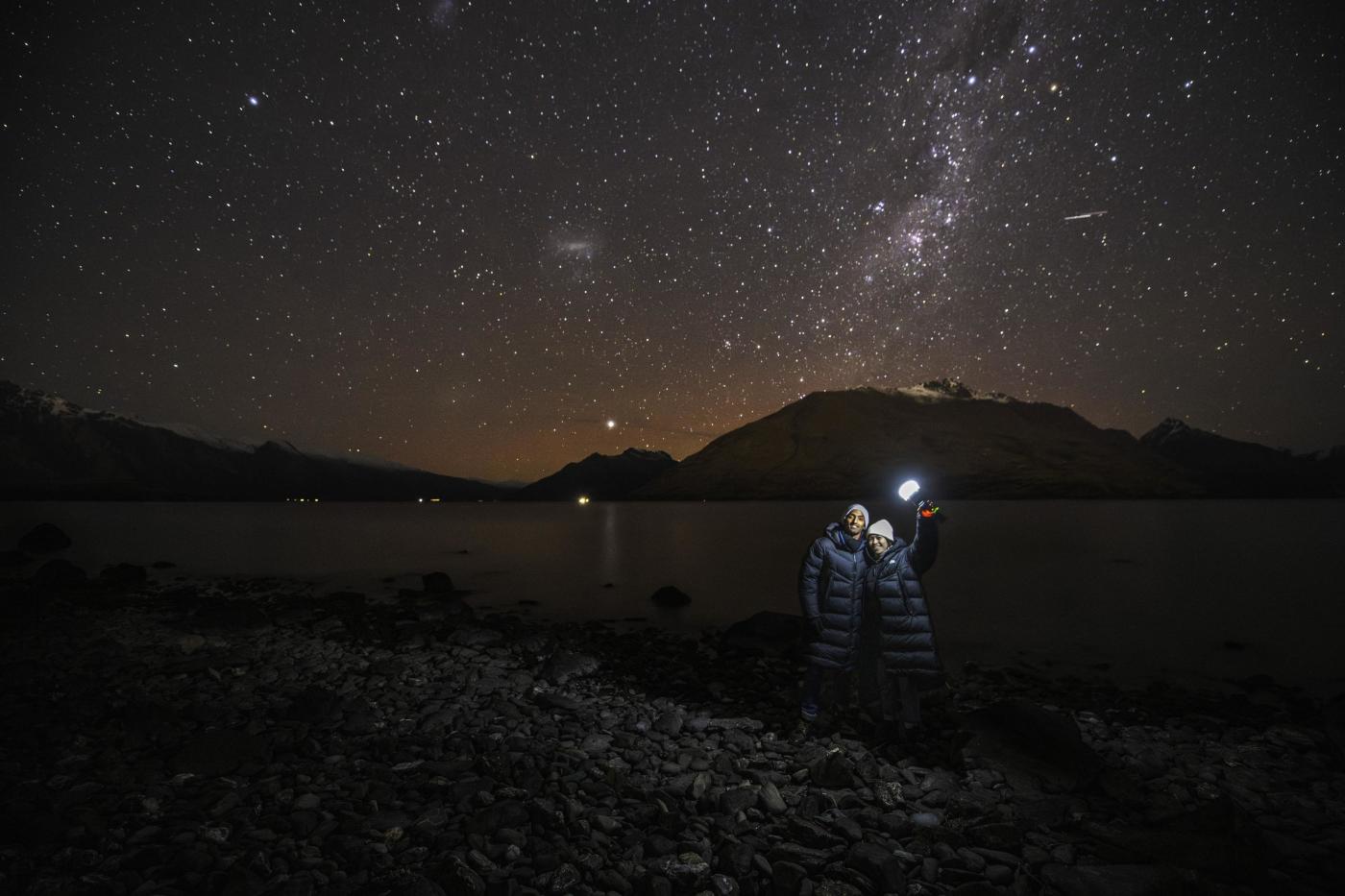 Two people holding a light with a background of mountains and a starry night sky