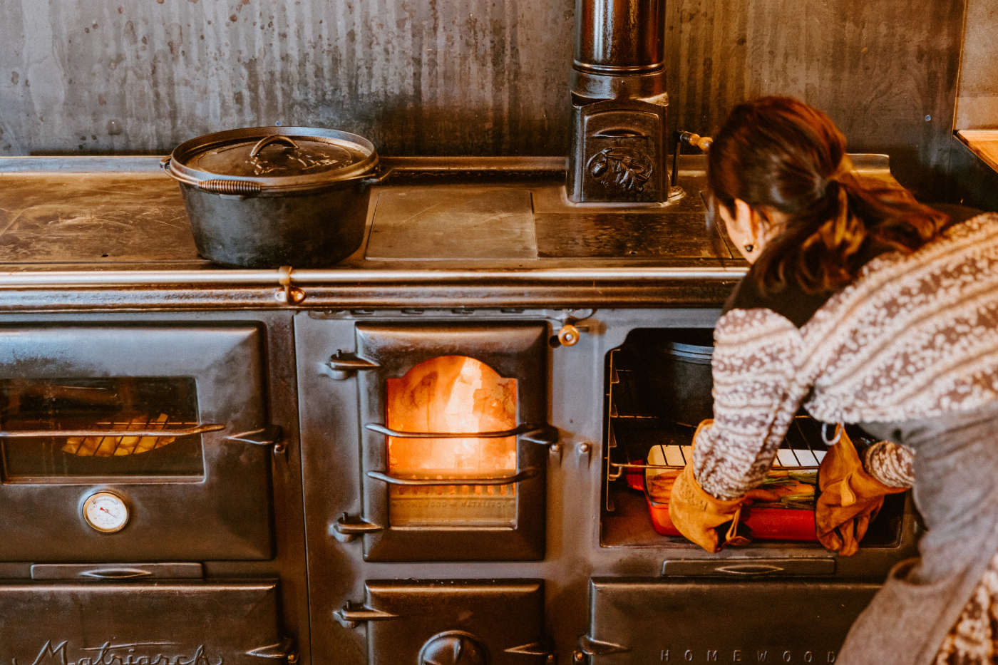 Woman cooking meal in cast iron pot over fire at The Great Glenorchy Alpine Base Camp restaurant