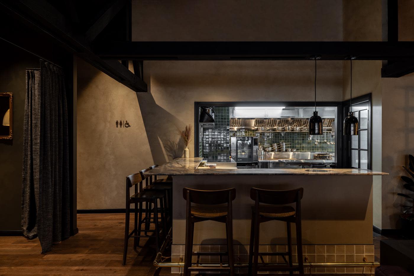 Inside setting of a dark and moody wine bar and restaurant with the kitchen pass in the background