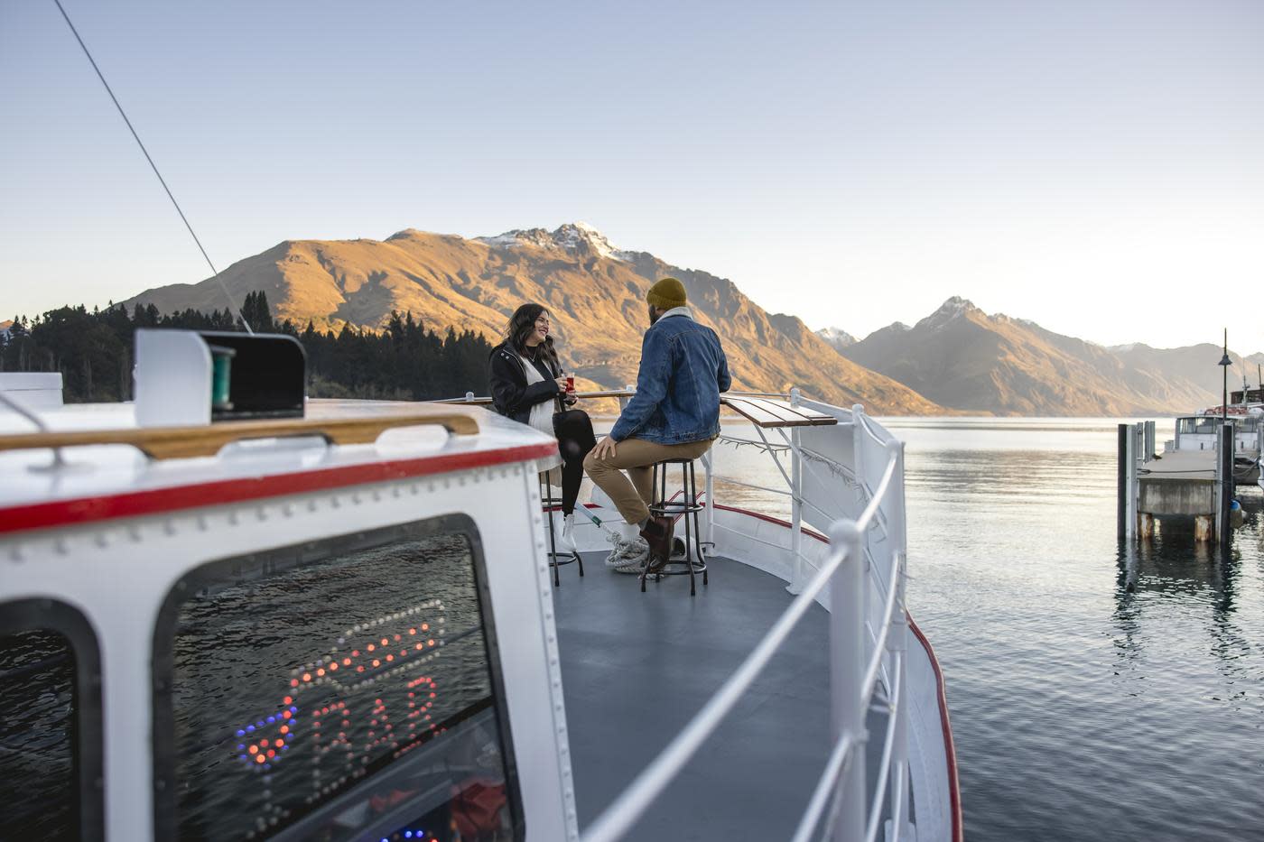 A couple sitting on the front of Perky's Floating Bar in Winter with lake and mountain views