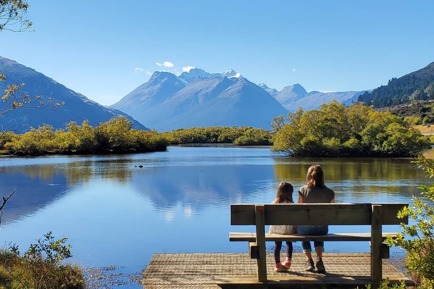 Mum and daughter sitting by lake with view of mountains in the background
