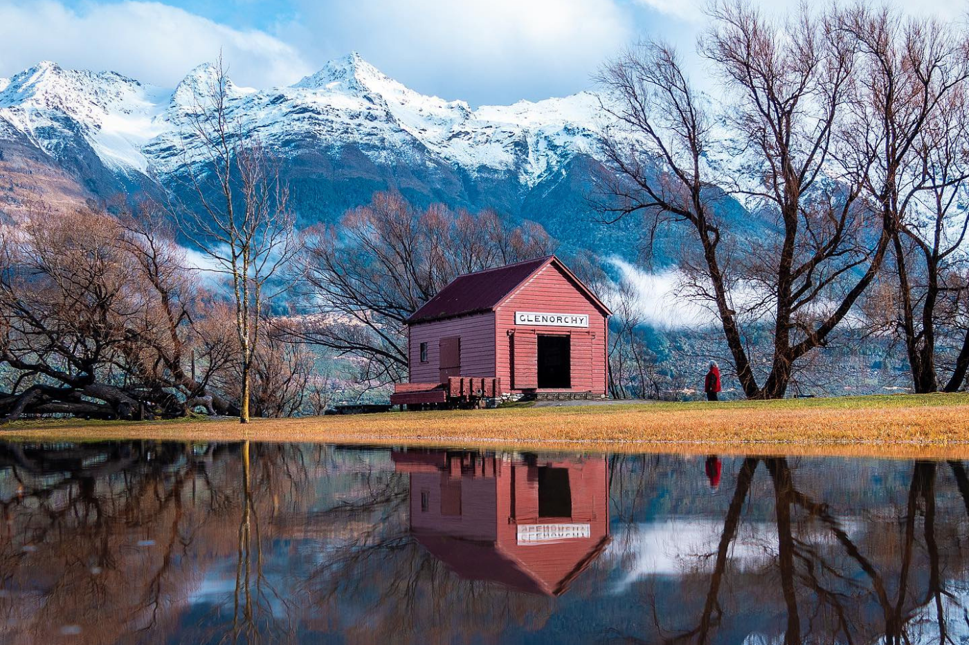 Red wharf shed and snowy mountains reflecting on the river