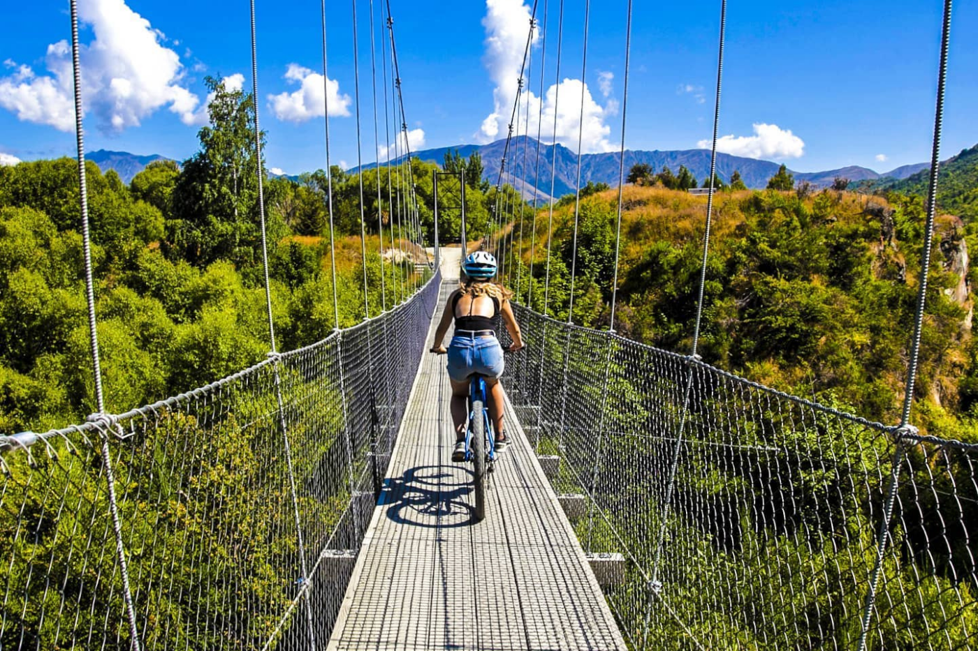 Girl riding bike over suspension bridge on Arrow River Bridges Trail