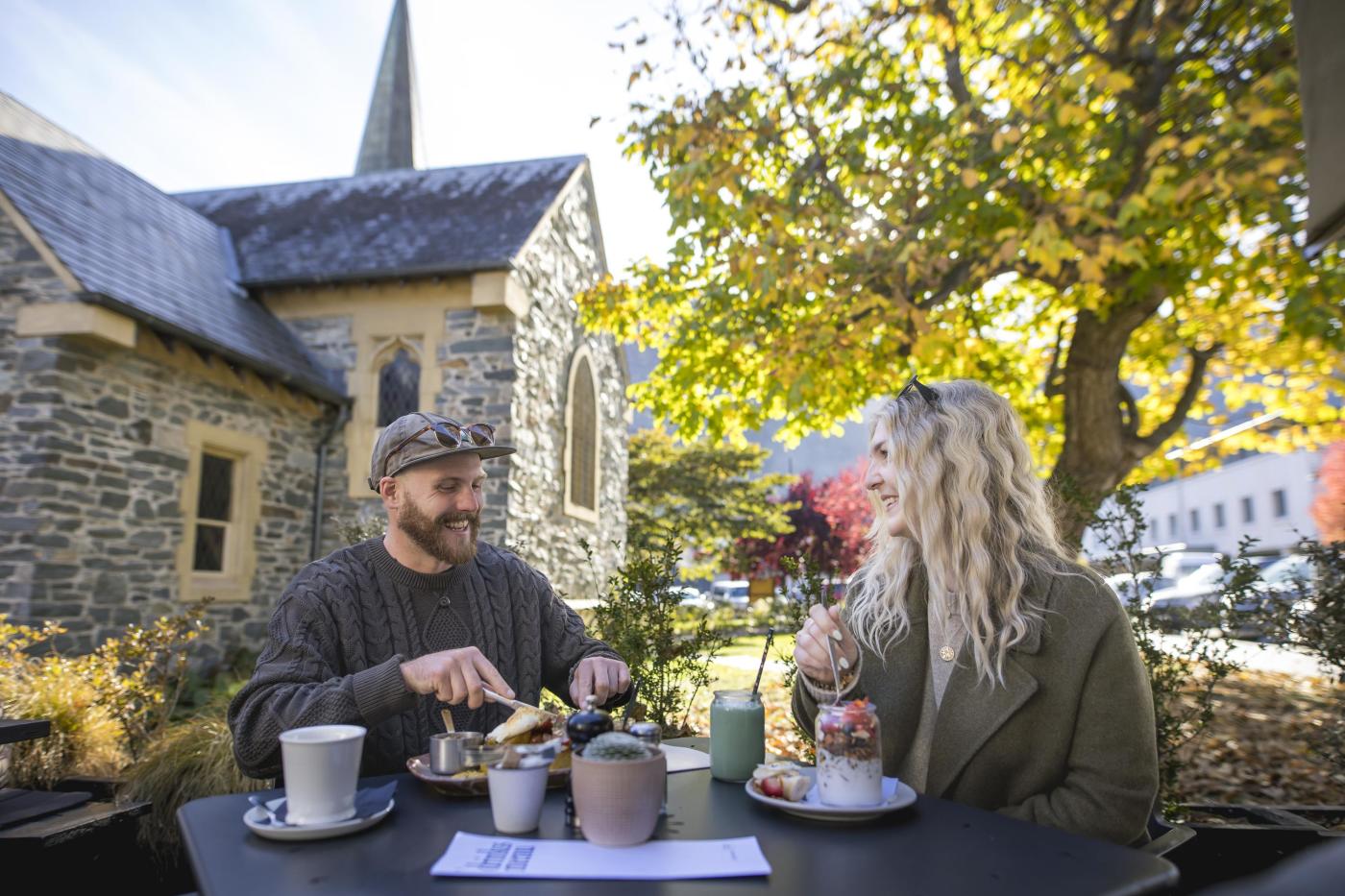 two people dining outside with a tree and church in the background