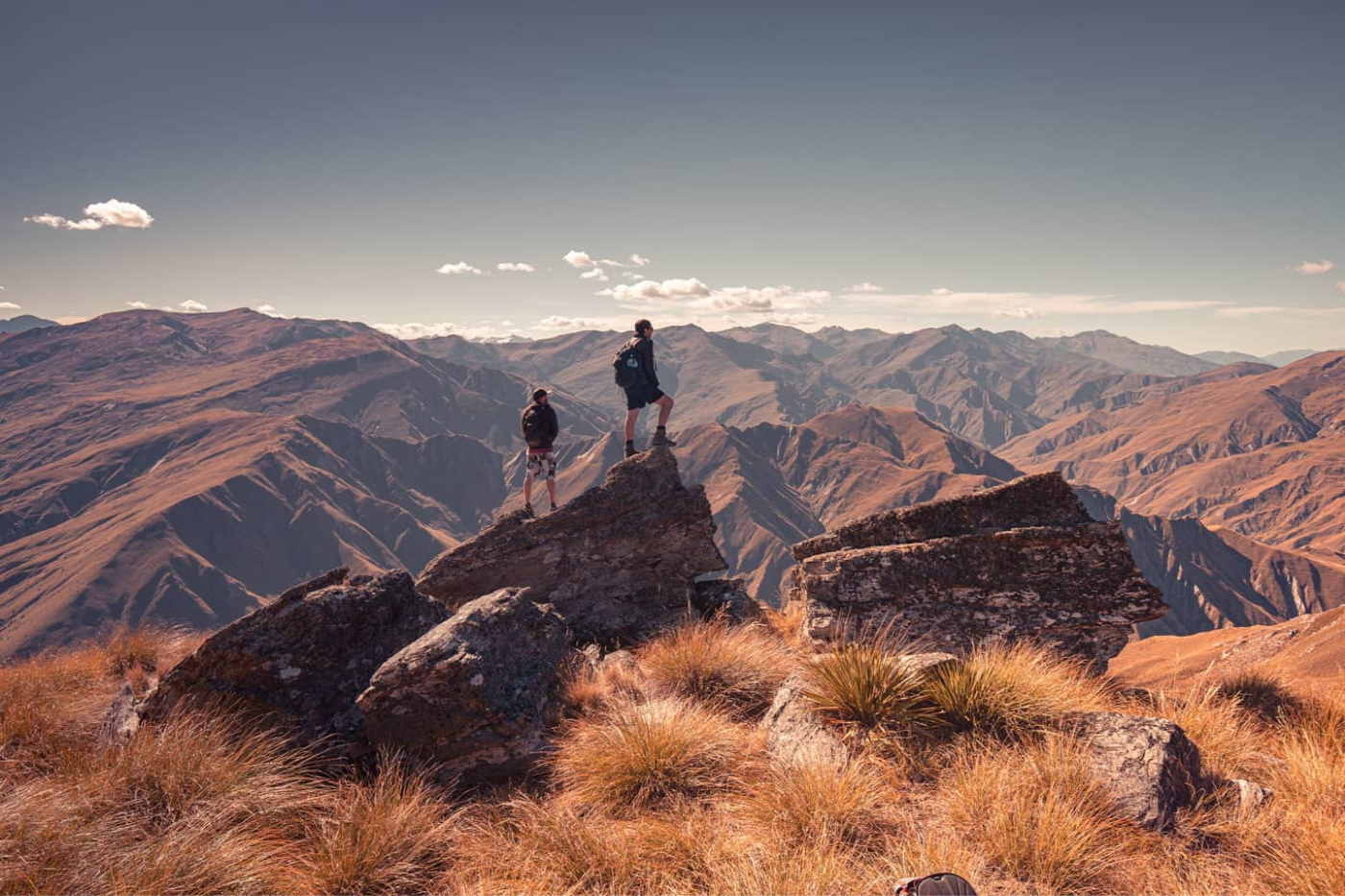 Two men standing atop of Brow Peak overlooking red rugged mountain ranges