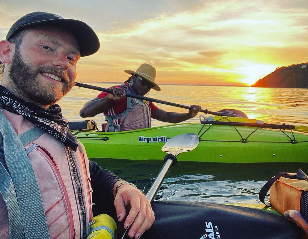 Two men pose while paddling kayaks off Mackinac Island at sunset