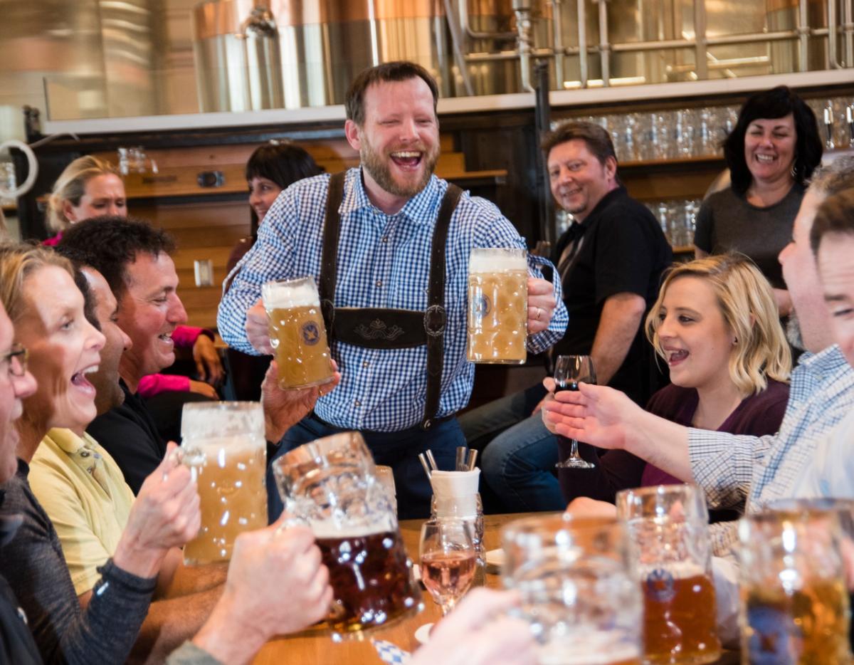 Man in lederhosen serving two liter steins to a group of smiling people at the Bavarian Bierhaus