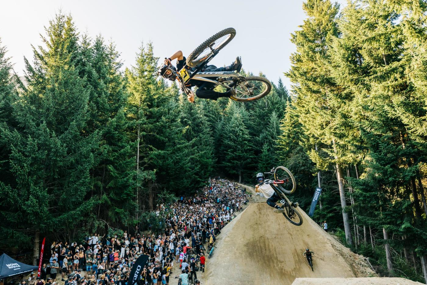 Two mountain bikers getting air over a big jump in front of a crowd at the Queenstown Bike Festival