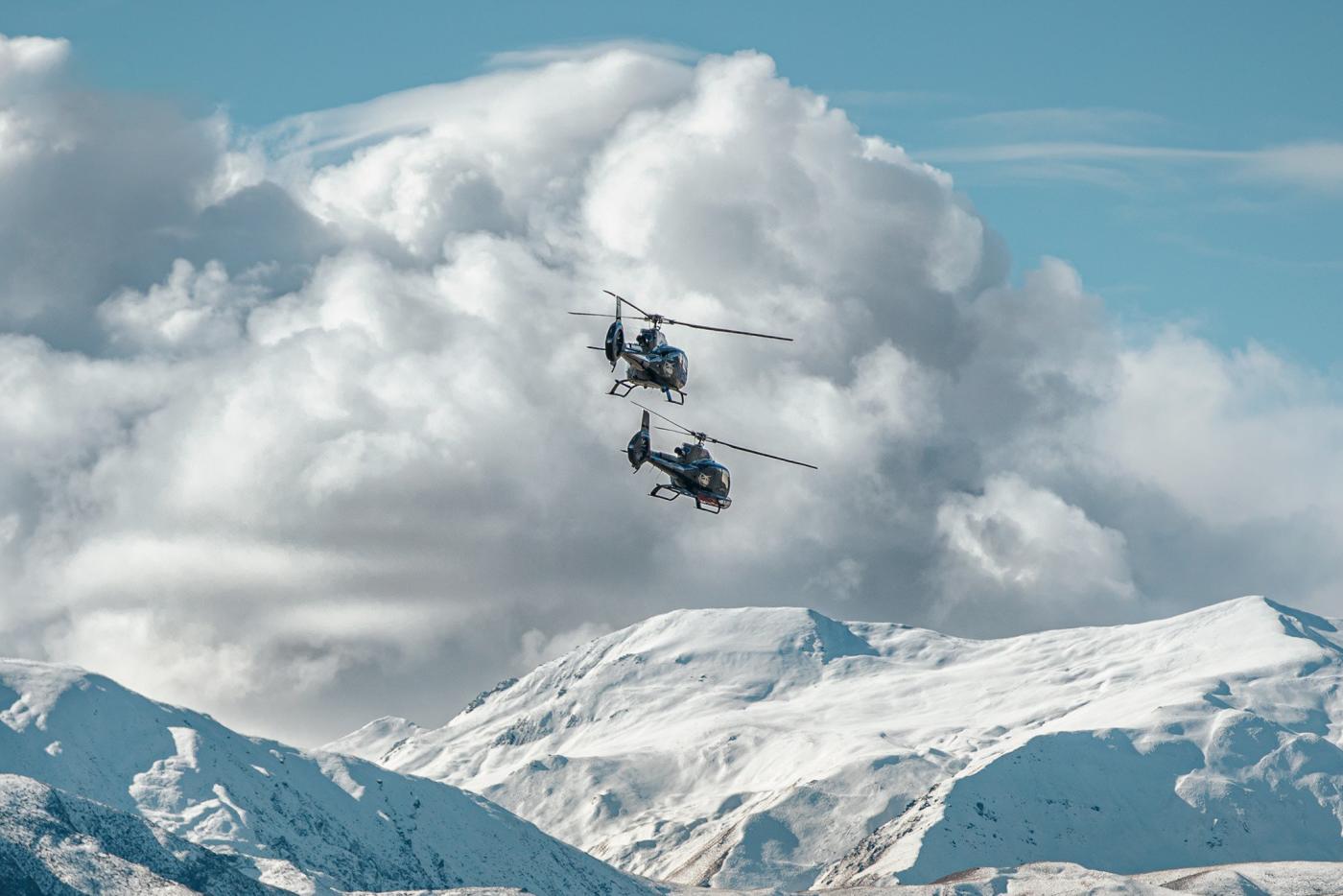 Two Over the Top Helicopters flying over snow covered mountains in winter