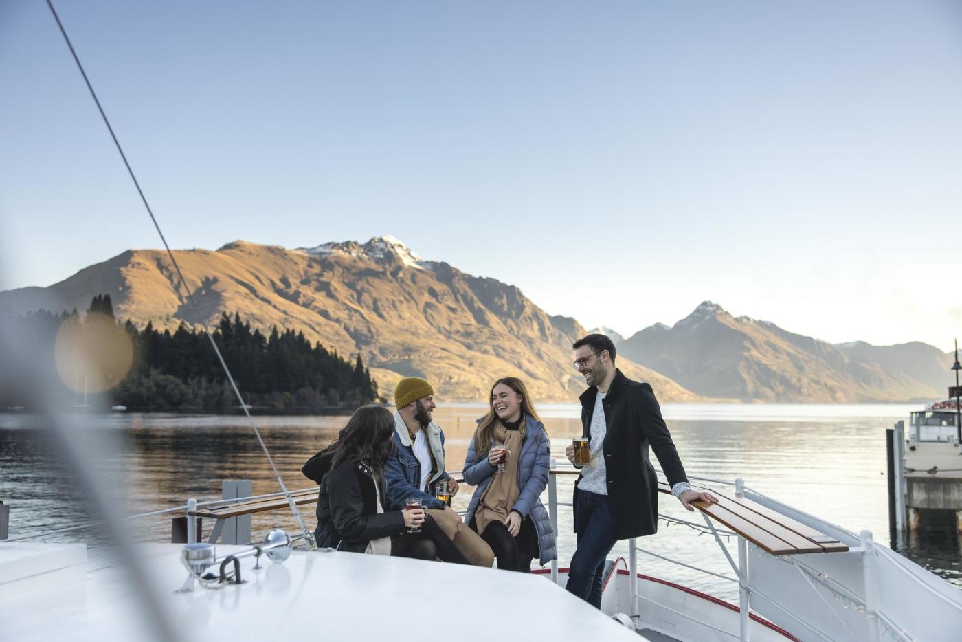 Friends sitting together at a bar on a boat with still lake and mountains in the background