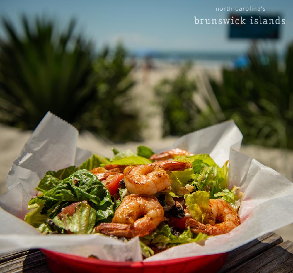 a salad with shrimp in a red basket on a table by the beach