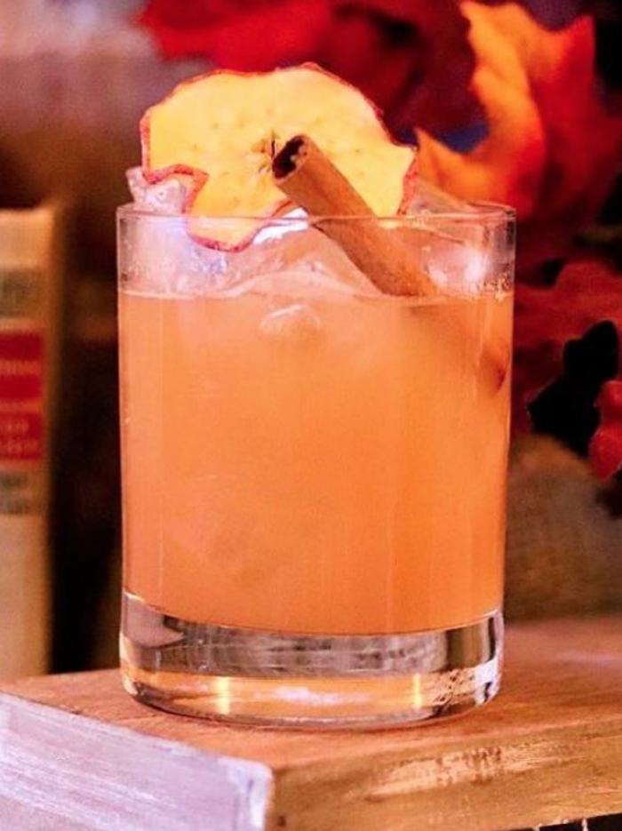 Cocktail glass with pink drink garnished with an apple slide and cinnamon stick