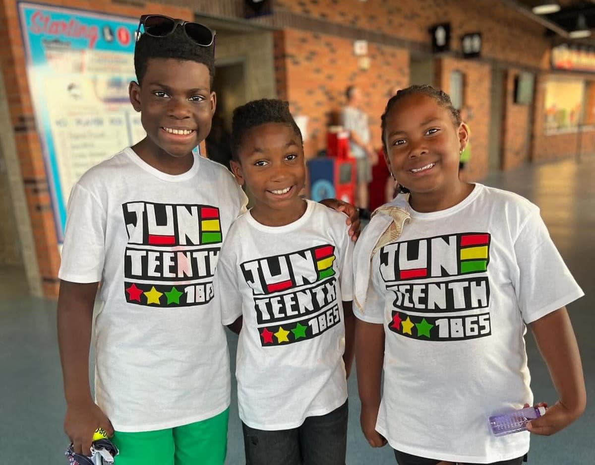 Three kids with Juneteenth shirts on at Kannapolis Cannon Ballers Stadium