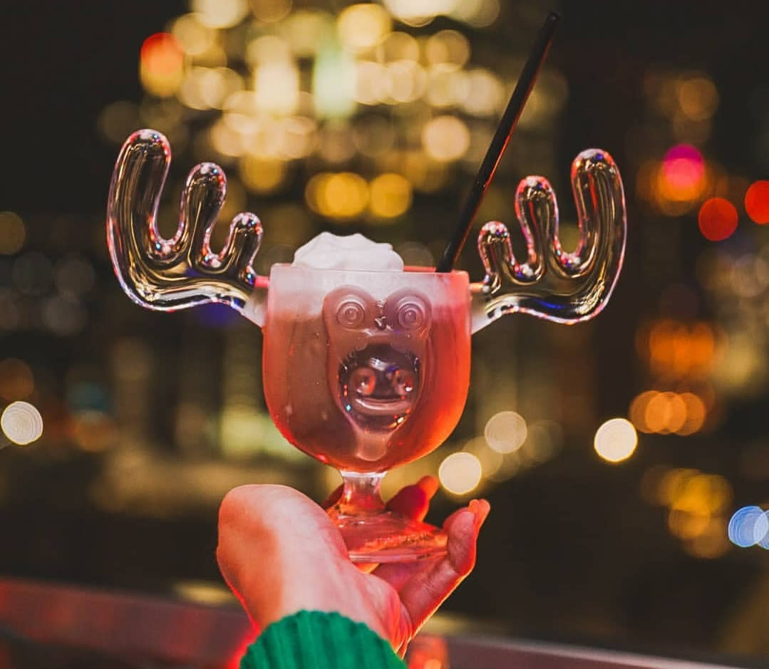Imagee of a hand holding out a cocktail in a glass shaped like a reindeer head and antlers.