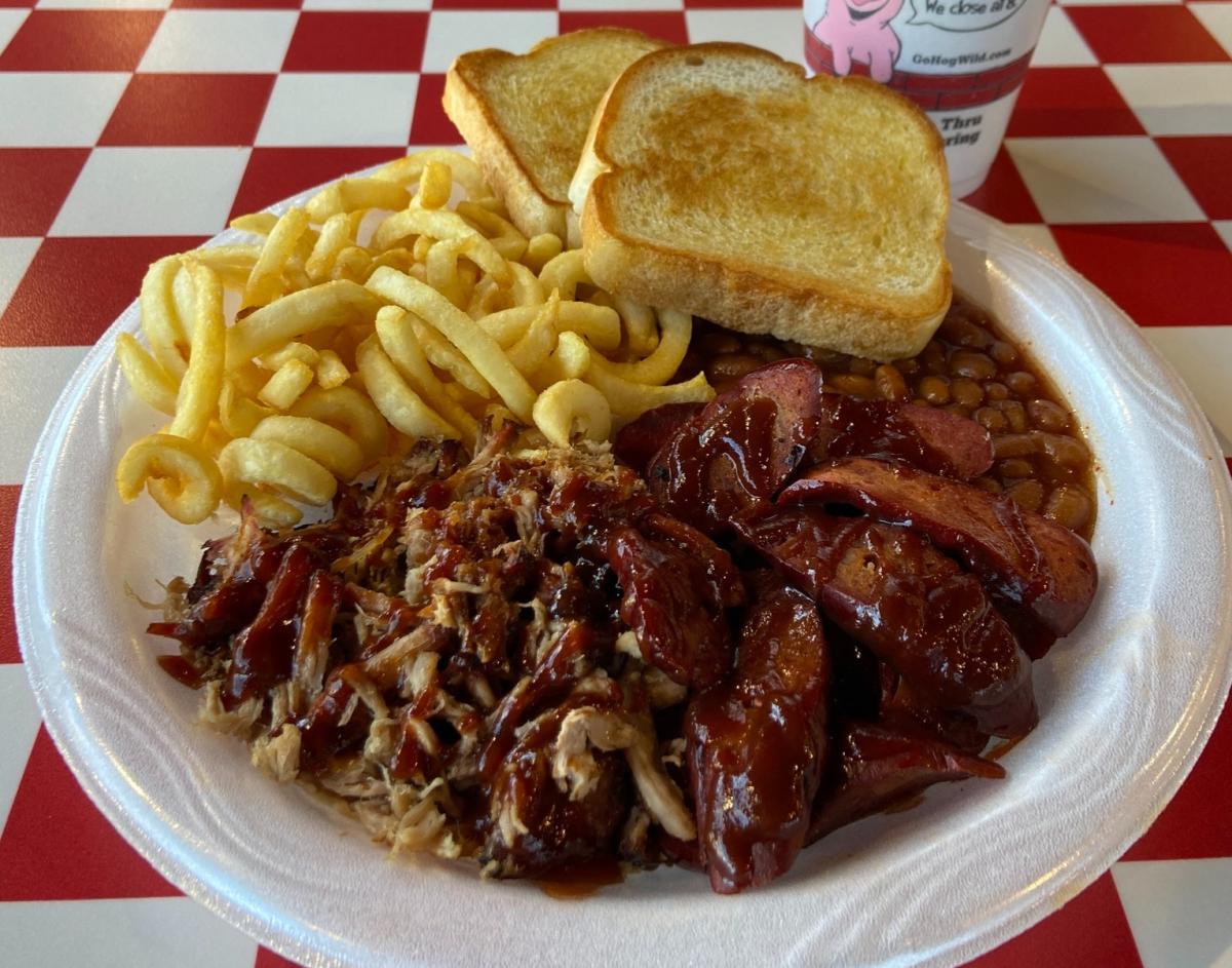 A plate of meat and sides is served on a paper plate at Hog Wild