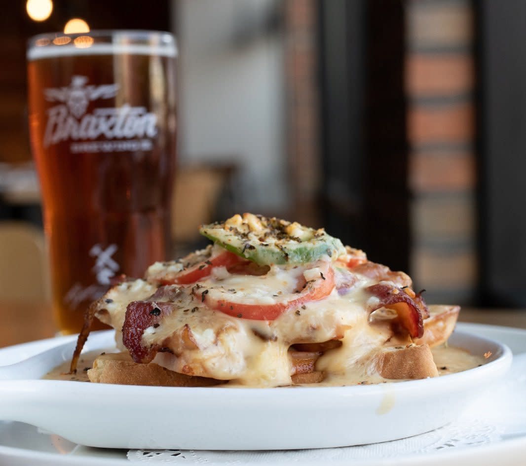 A hot brown sandwich on a white plate with a glass of Braxton craft beer at Parlor on Seventh restaurant