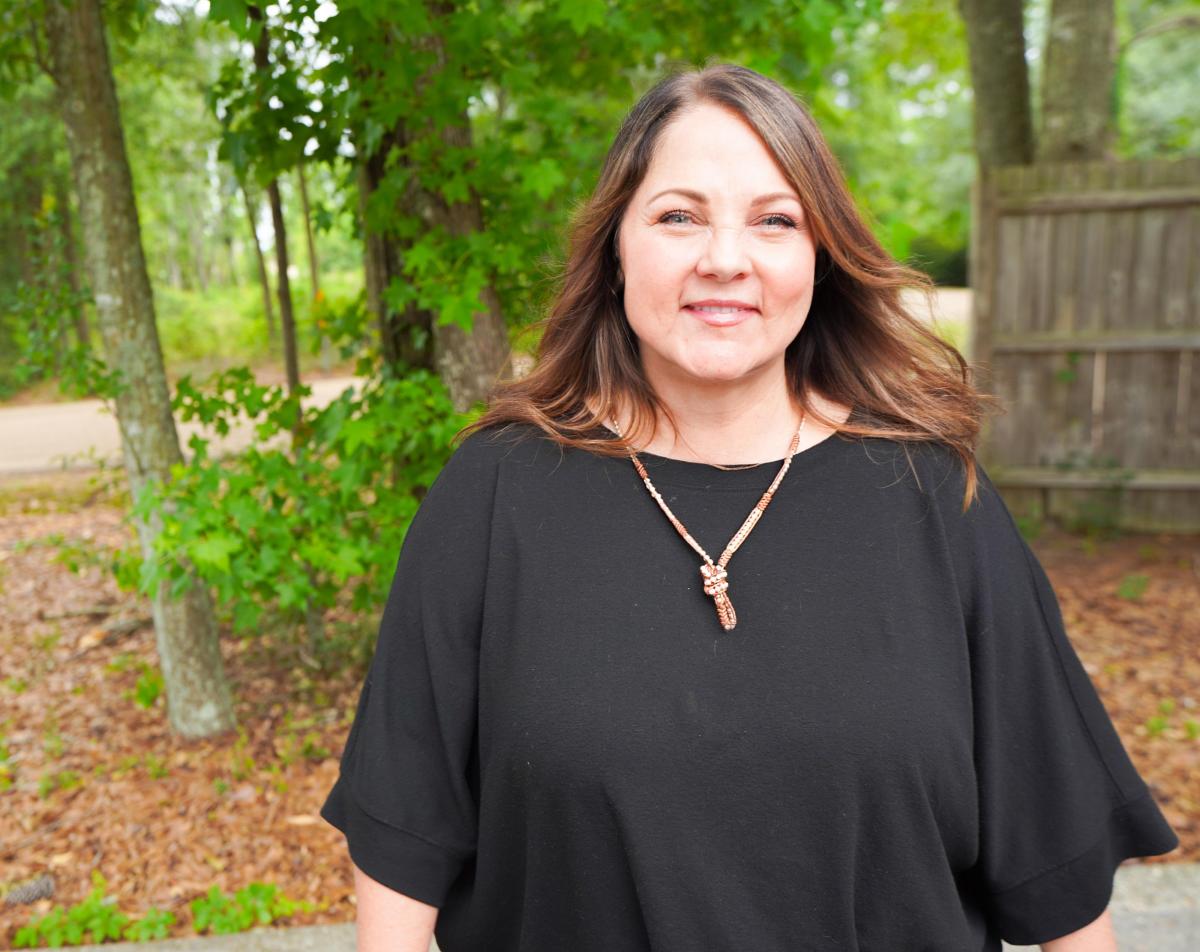 City of Covington's Director of Cultural Arts & Events, Sarada Bonnett. She is wearing a black shirt, smiling, and surrounded by trees.