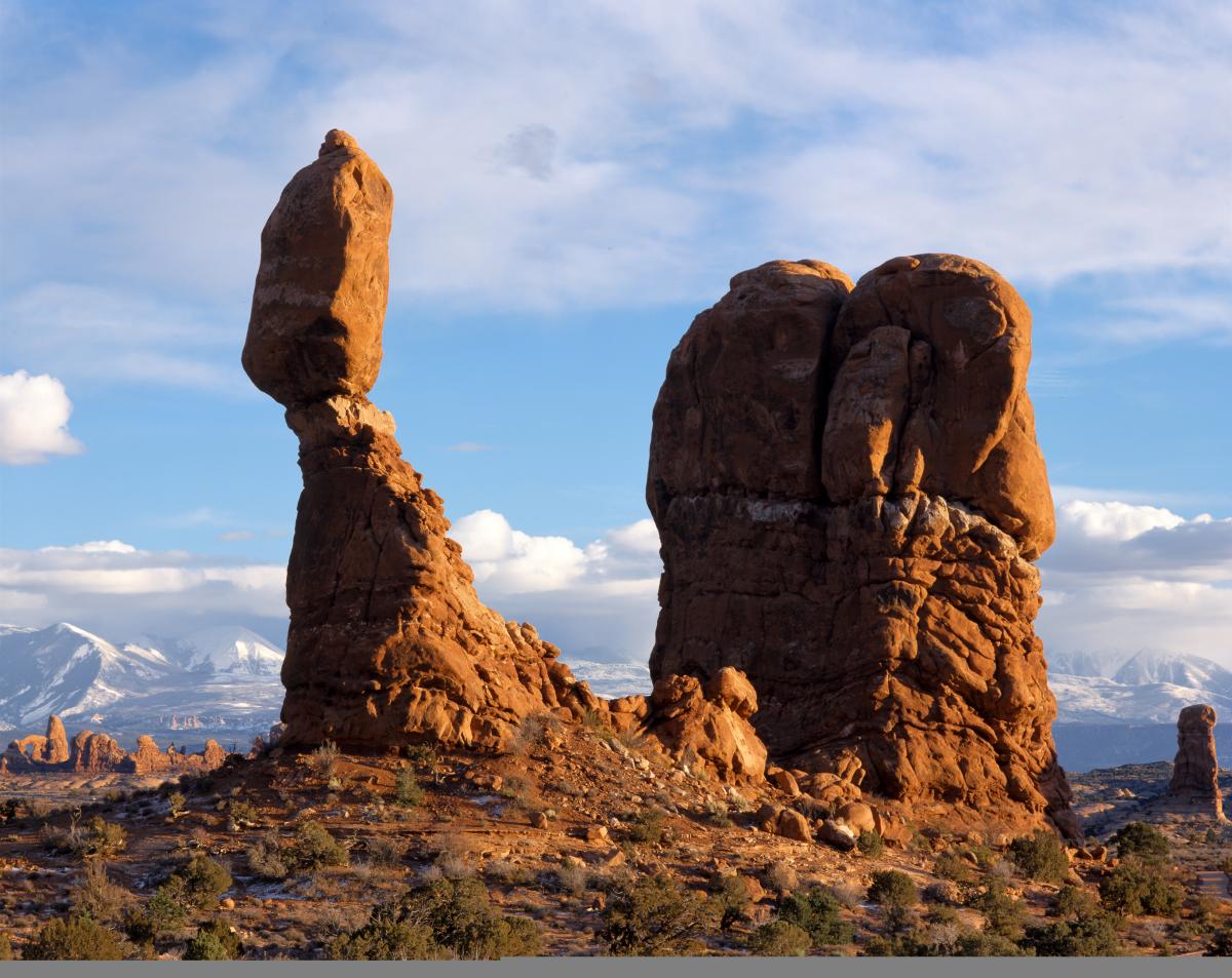 Balanced Rock formation standing above the surrounding red rock desert with blue skies and distant snow-capped mountains.