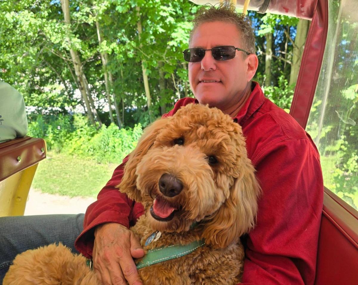 A man holds his dog on the seat of a horse-drawn carriage tour of Mackinac Island