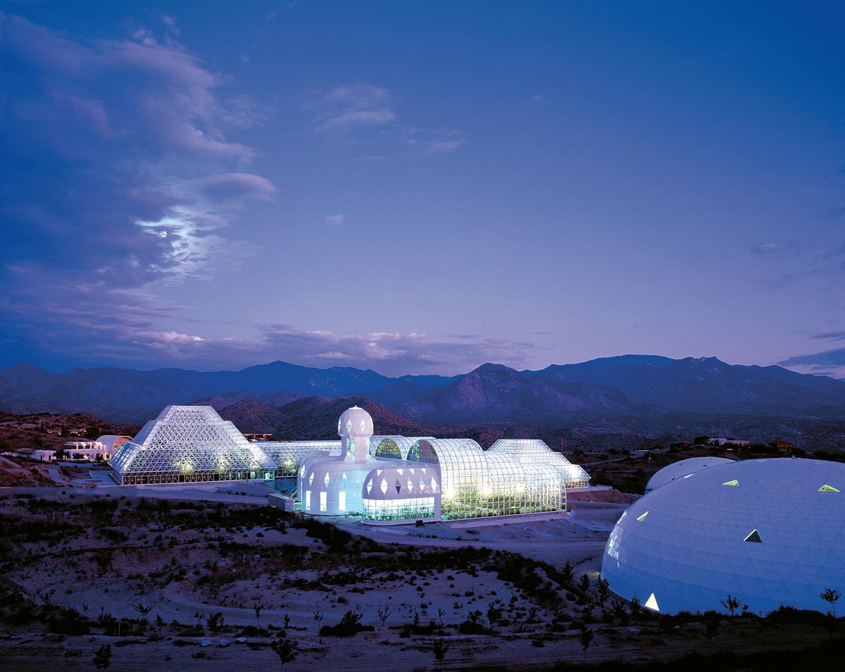 Photo of the Biosphere 2, several white buildings in organic shapes with numerous lit windows, from a distance at night