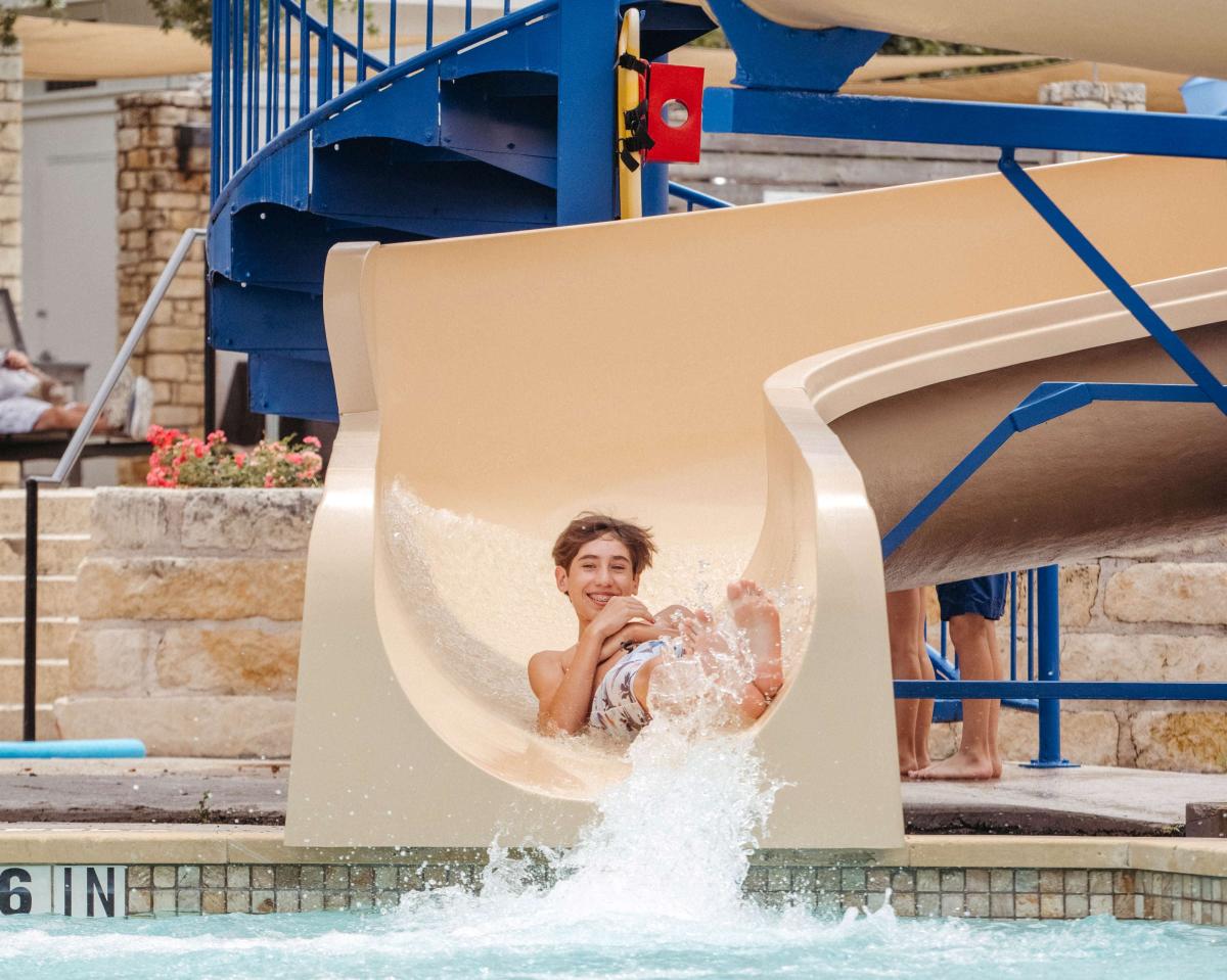 A boy sliding down a water slide into a pool of water.