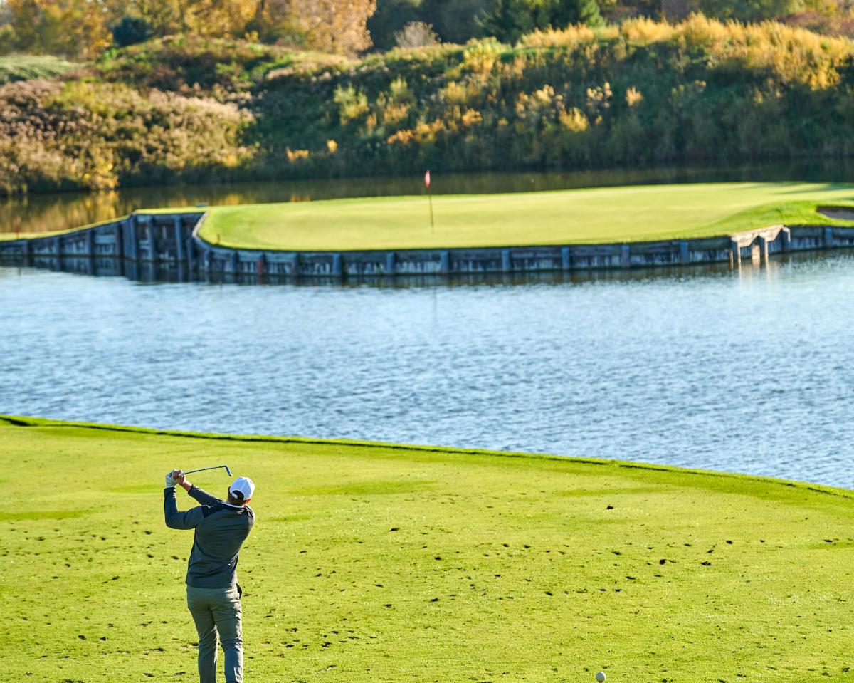 Golfer hitting ball across water to the putting green.