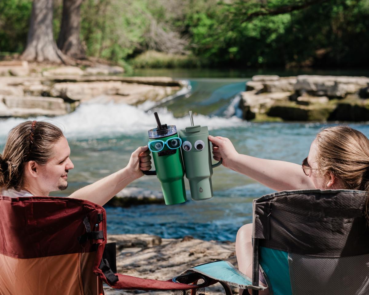 A couple cheers their fun reusable containers on the banks of the San Marcos River.
