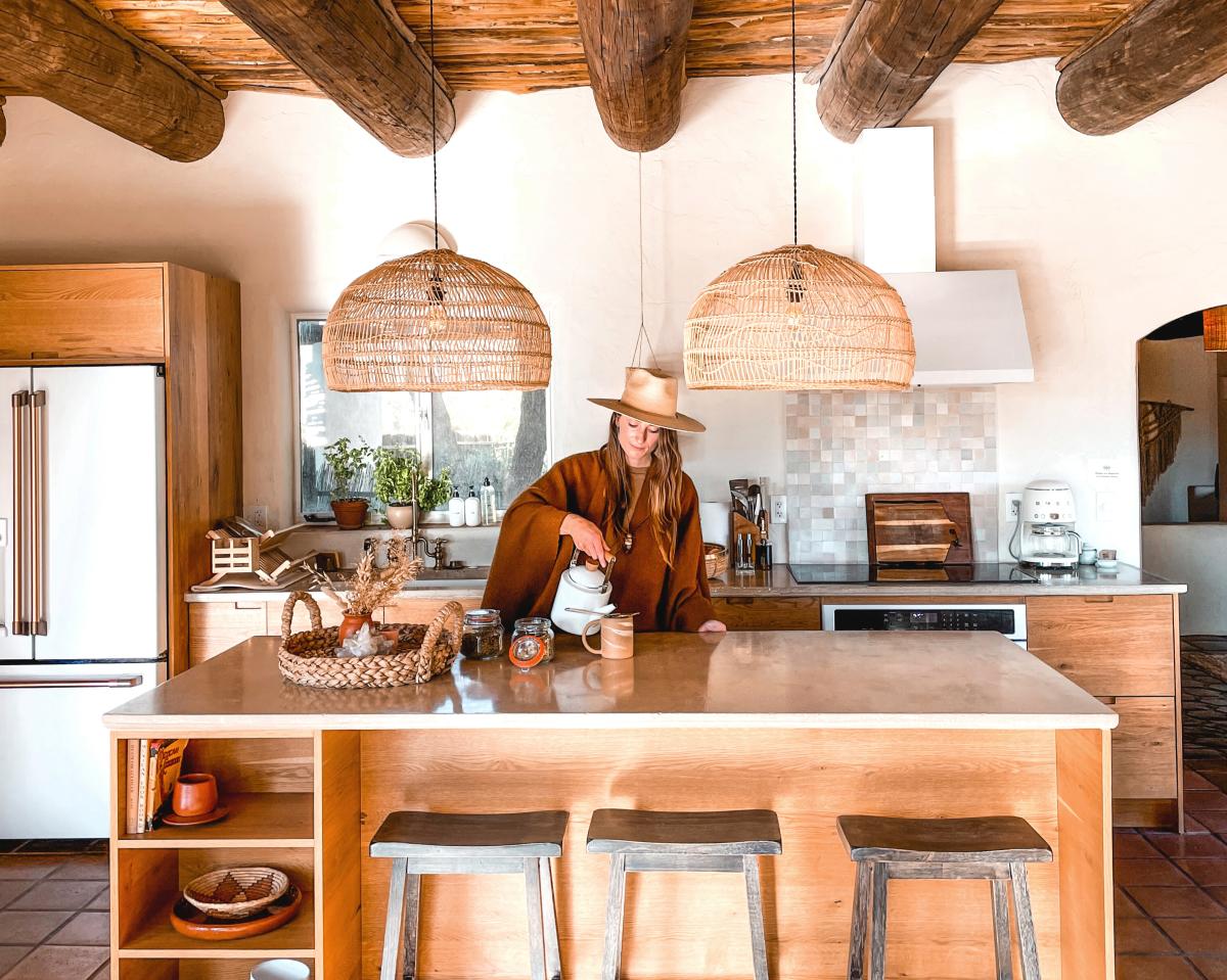 Woman standing at Kitchen Island pouring into a mug from a kettle