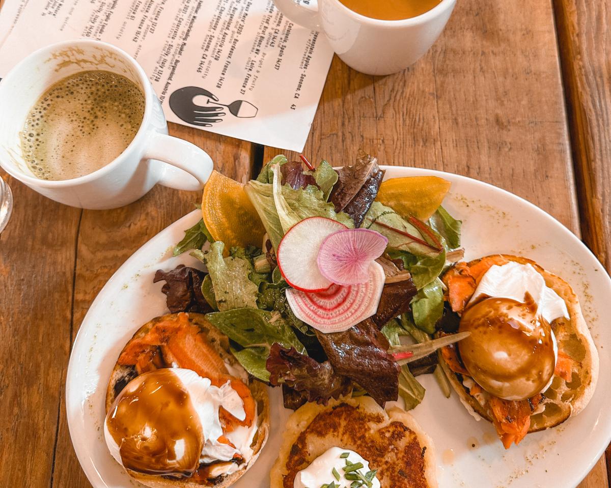 Ariel shot of eggs Benedict breakfast with side salad and two mugs with 5 points menu on table