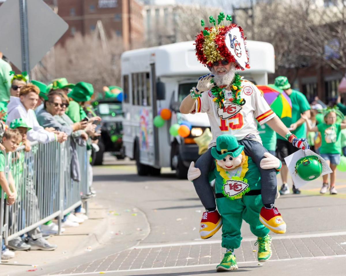 A man wearing green and kansas city chiefs attire walks through the Paddy Day Parade in Delano