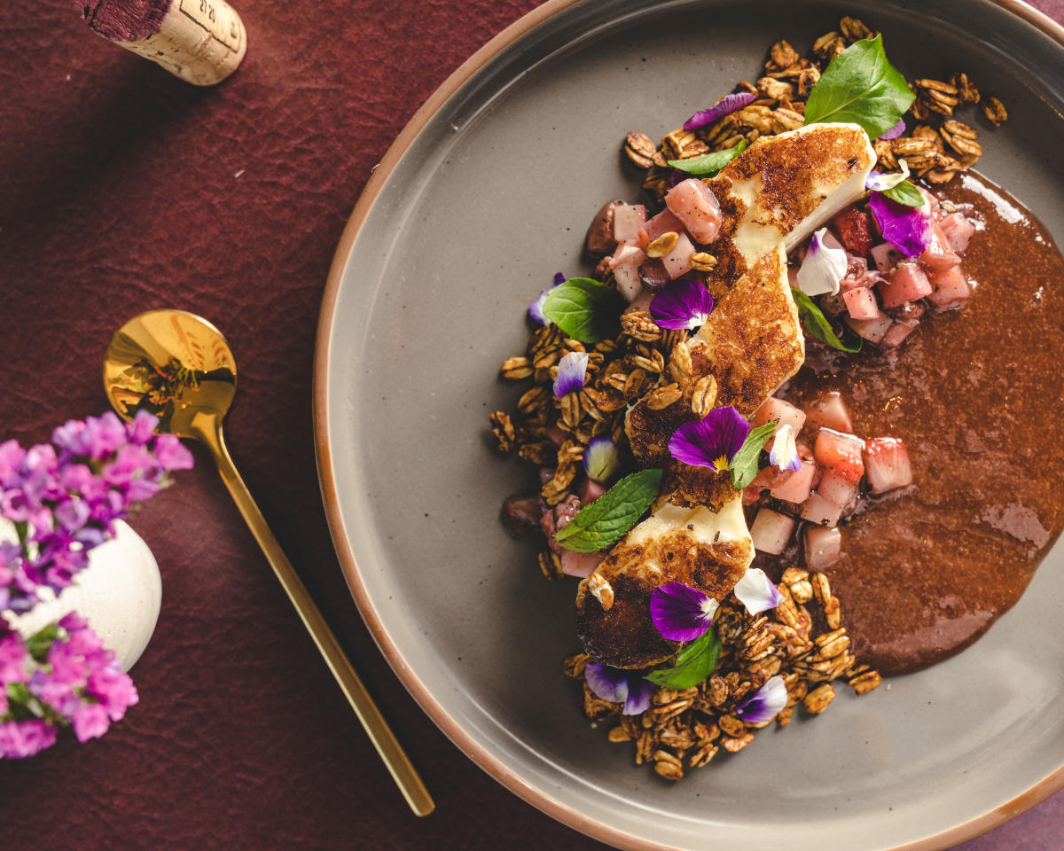 Image of a plate of food displayed beautifully with flowers and a golden spoon sitting next to the plate on the table.